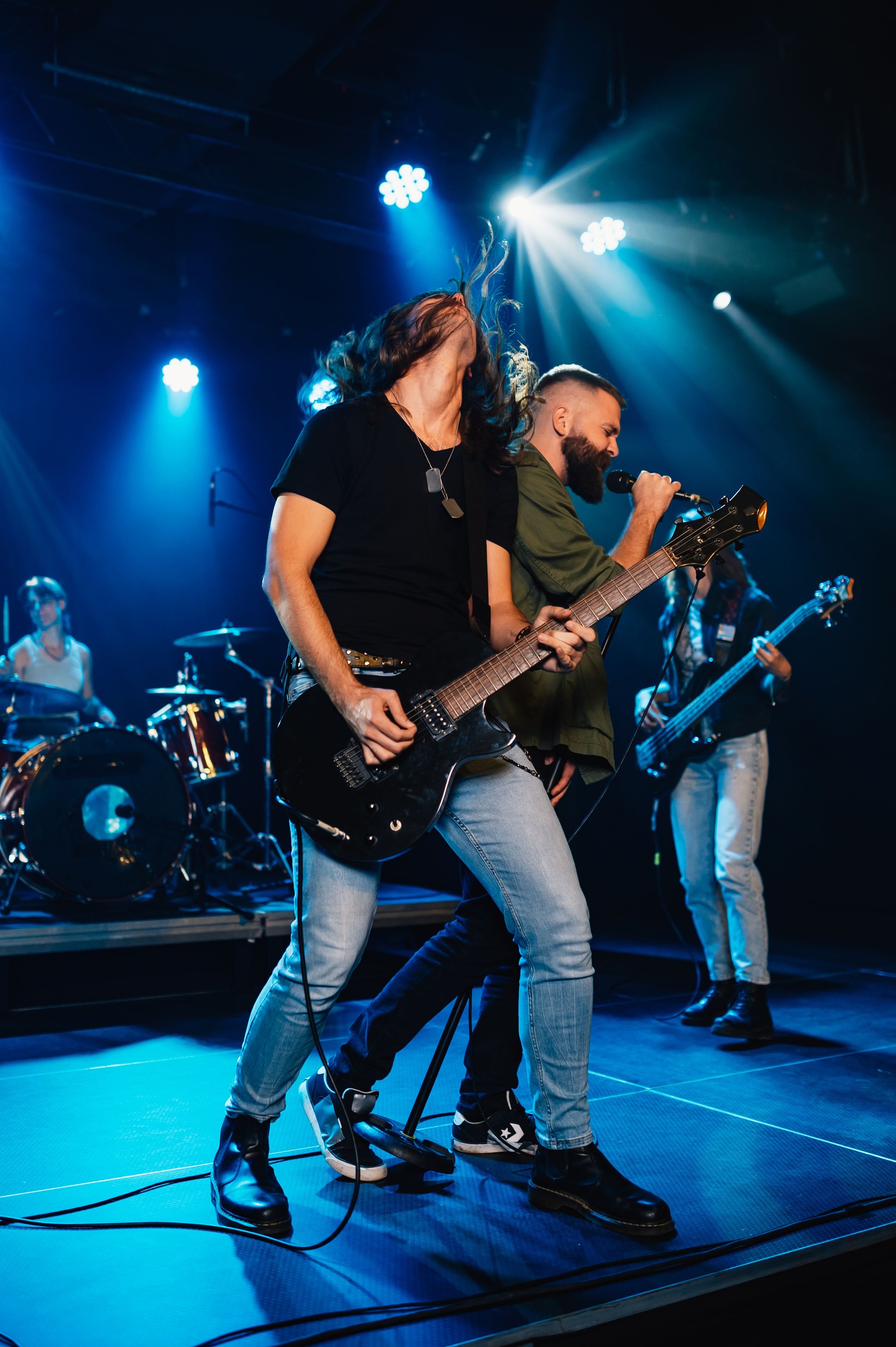 Rock band performing energetically on stage under blue lights